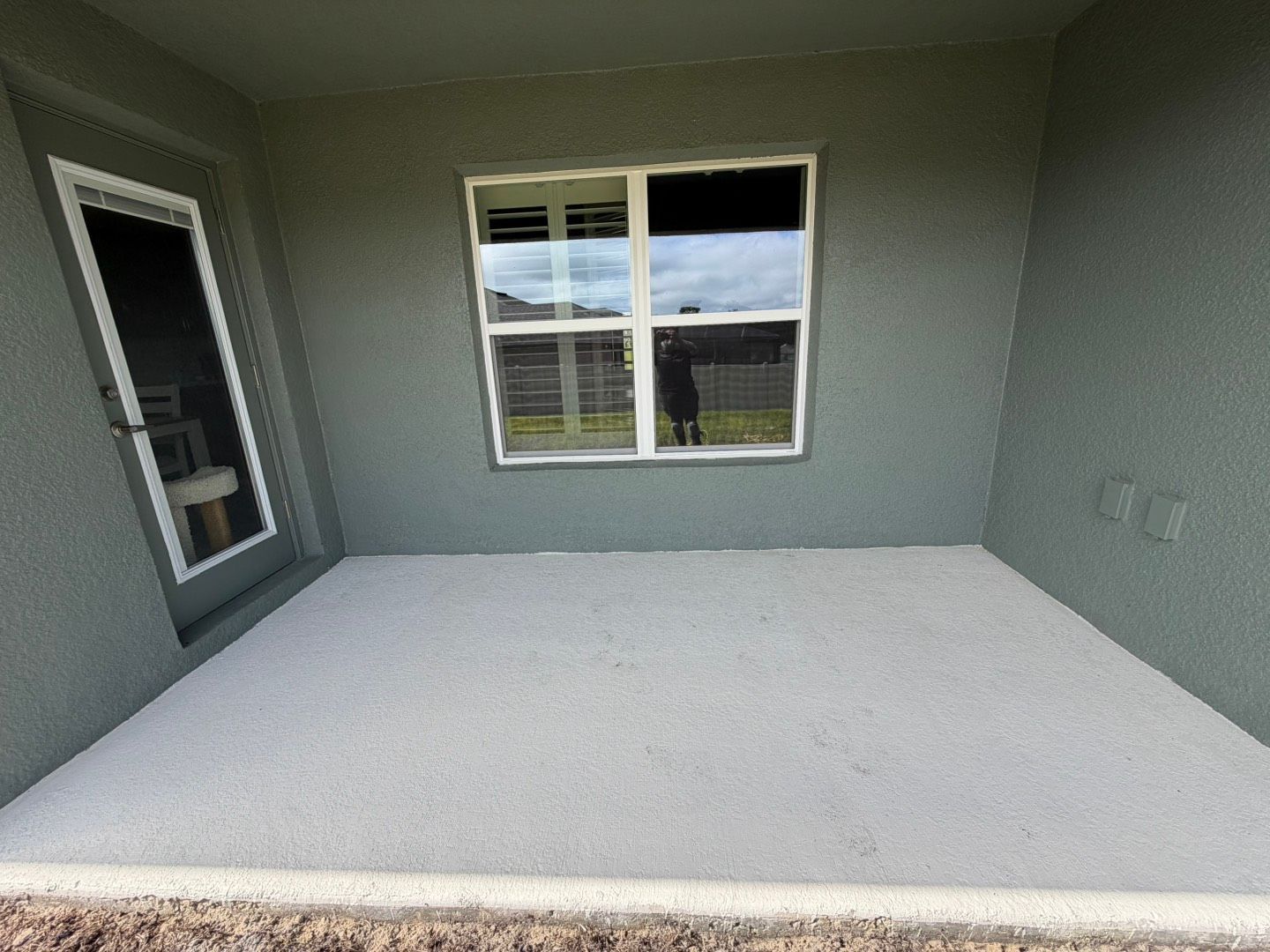 Empty gray carpeted room with a window and a door, viewed from the corner.