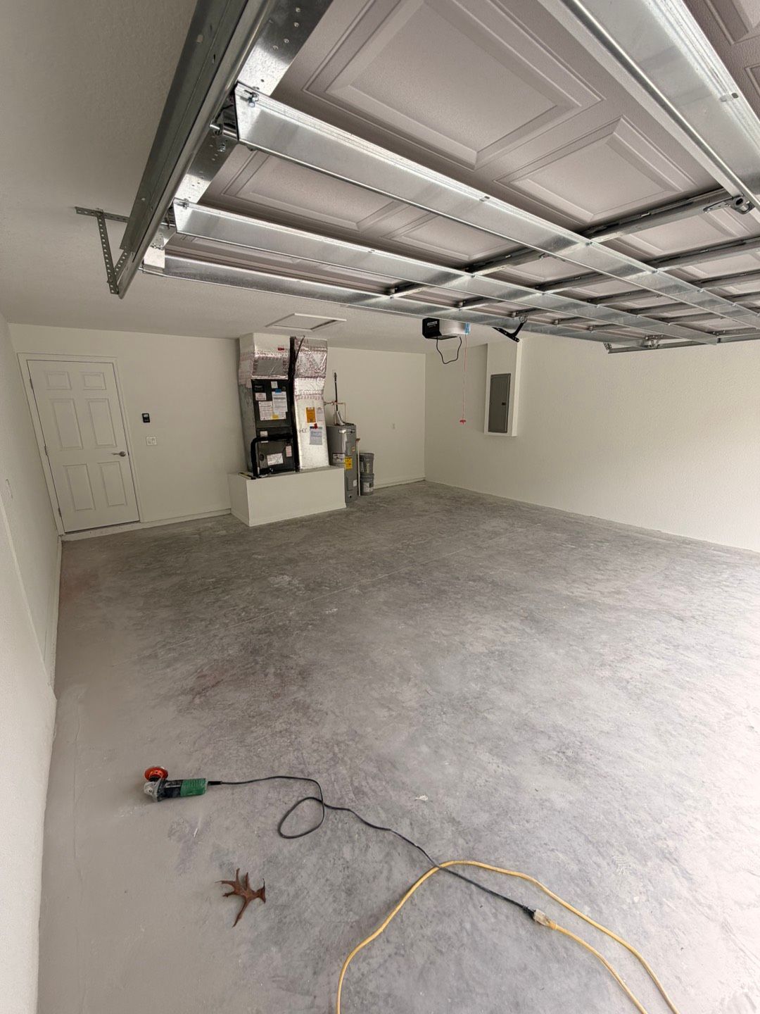 Empty garage with concrete floor, open overhead door, and tools on the floor.