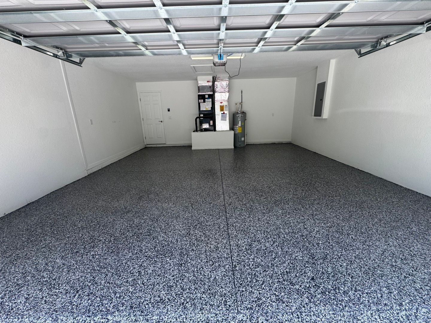 Empty garage with gray speckled floor, white walls, and a closed ceiling door opener.