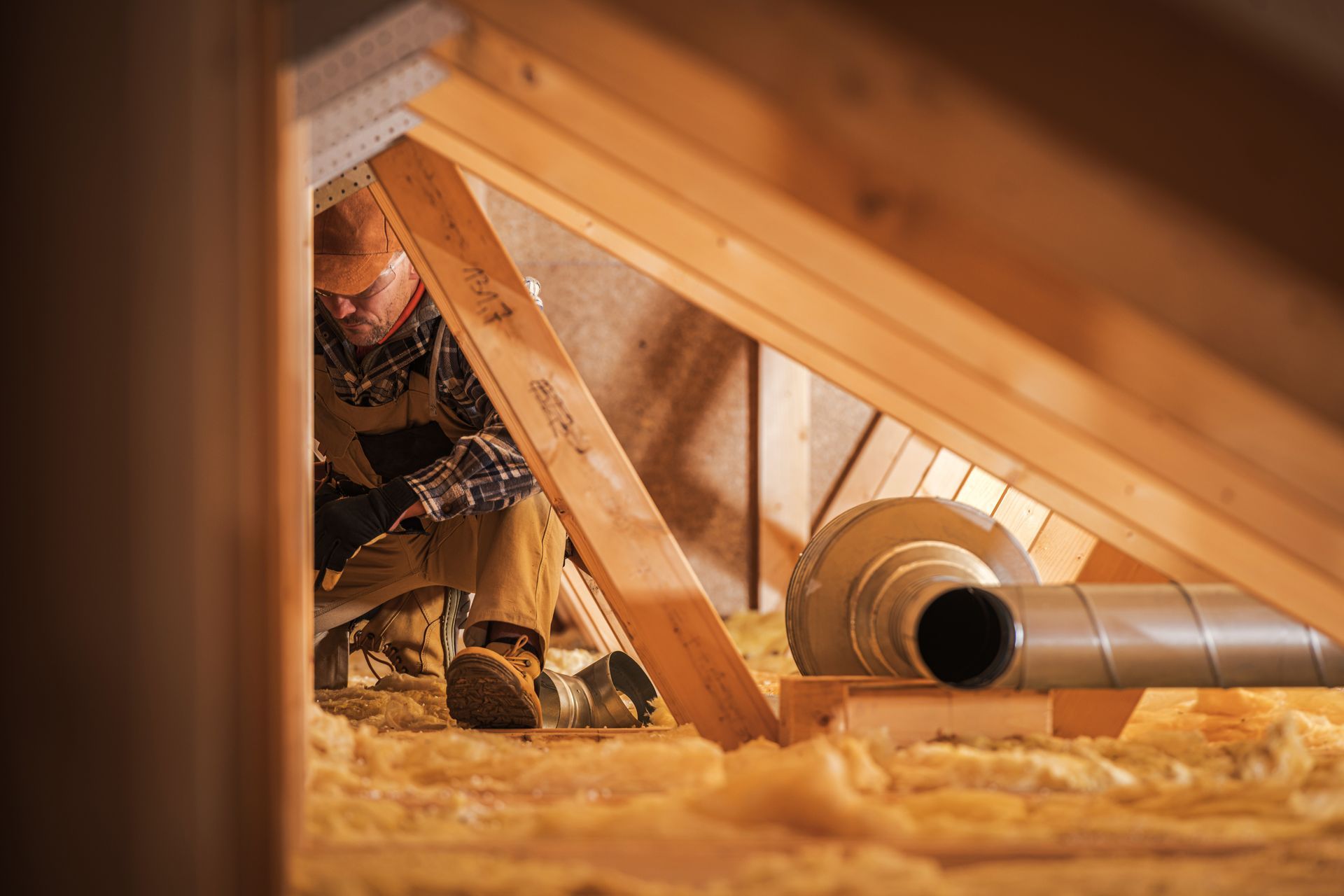 Man working in an attic, installing ventilation pipes among insulation.