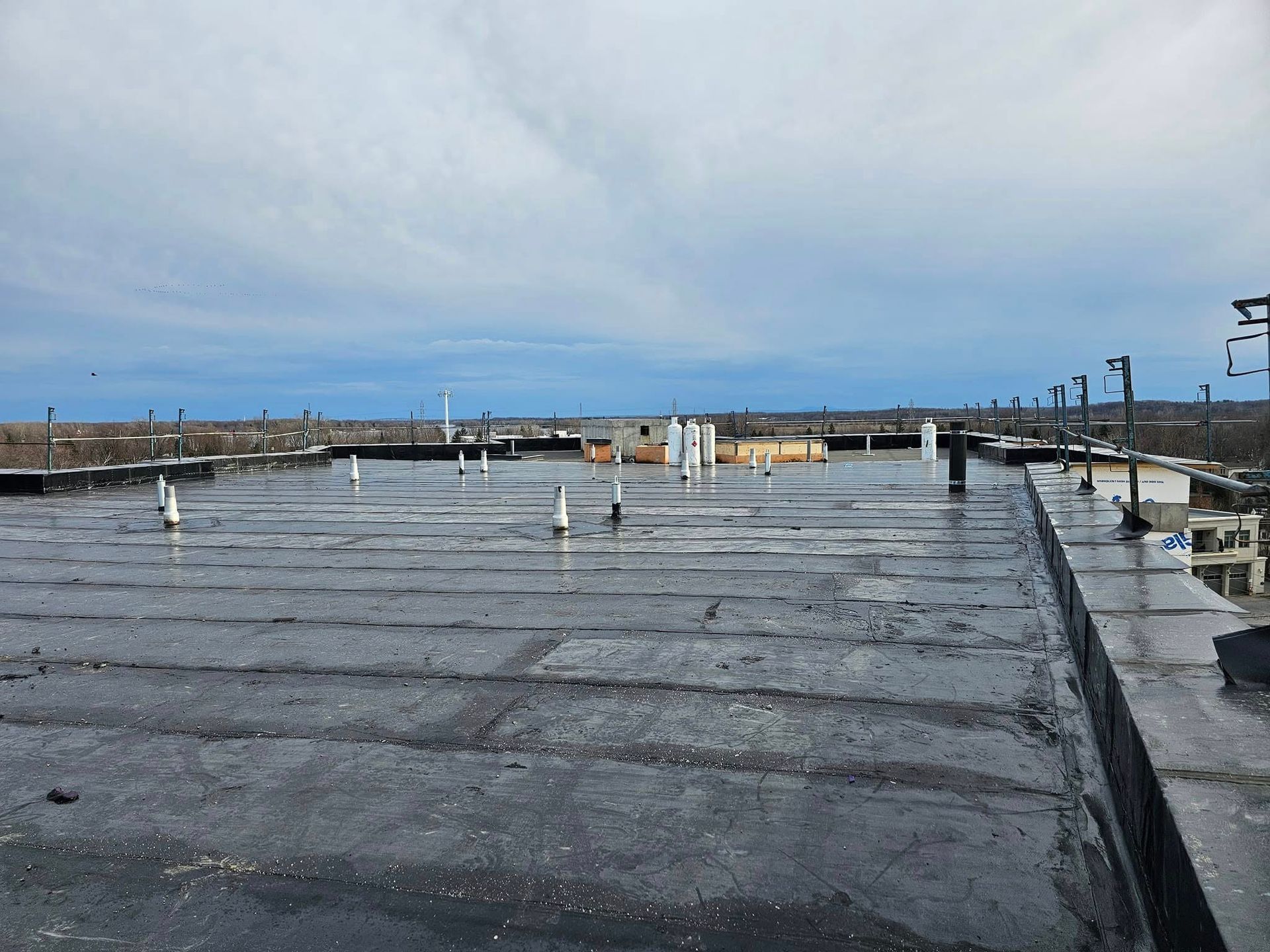 Toit plat et noir avec de multiples tuyaux blancs, ciel couvert en arrière-plan.