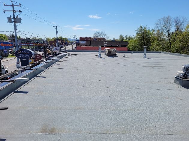 Flat commercial rooftop with vents, looking toward a road with buildings on a sunny day.