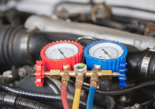 Red and blue AC manifold gauges attached to hoses on a car engine
