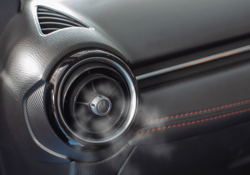 Close-up of a car’s circular dashboard air vent with black leather and red stitching accents