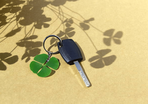 Key and green clover keychain on yellow background with leaf shadows