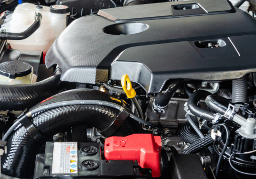 Close-up of a car engine bay with black cover, red battery terminal, and yellow dipstick