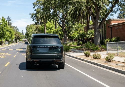 Dark green Range Rover driving through a school zone on a palm-lined street