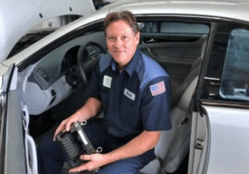 Mechanic in navy uniform sitting in a car, holding a black tool inside a garage