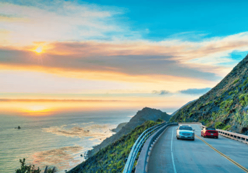 Coastal highway at sunset with cars driving beside the ocean and cliffs
