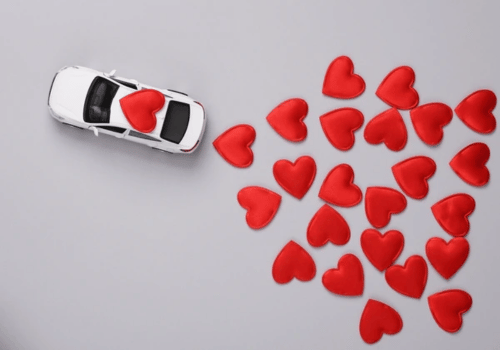 White toy car with a red heart beside a cluster of red heart shapes on a gray background