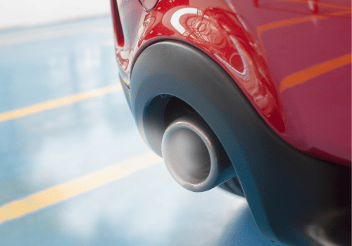 Close-up of a red car’s rear exhaust pipe with blue smoke on the pavement