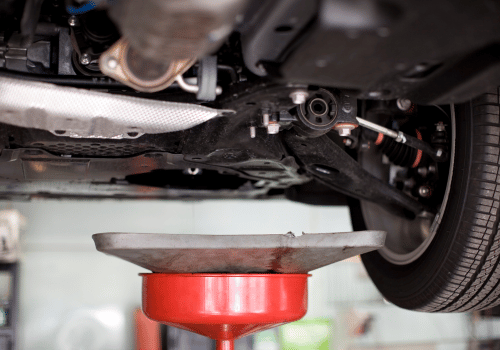 Car underside on a lift above a red oil drain pan during maintenance