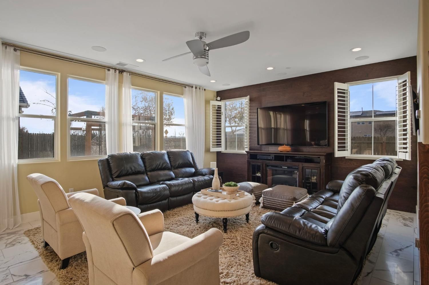 Living room with black leather couches, beige armchairs, and a TV on a brown accent wall.