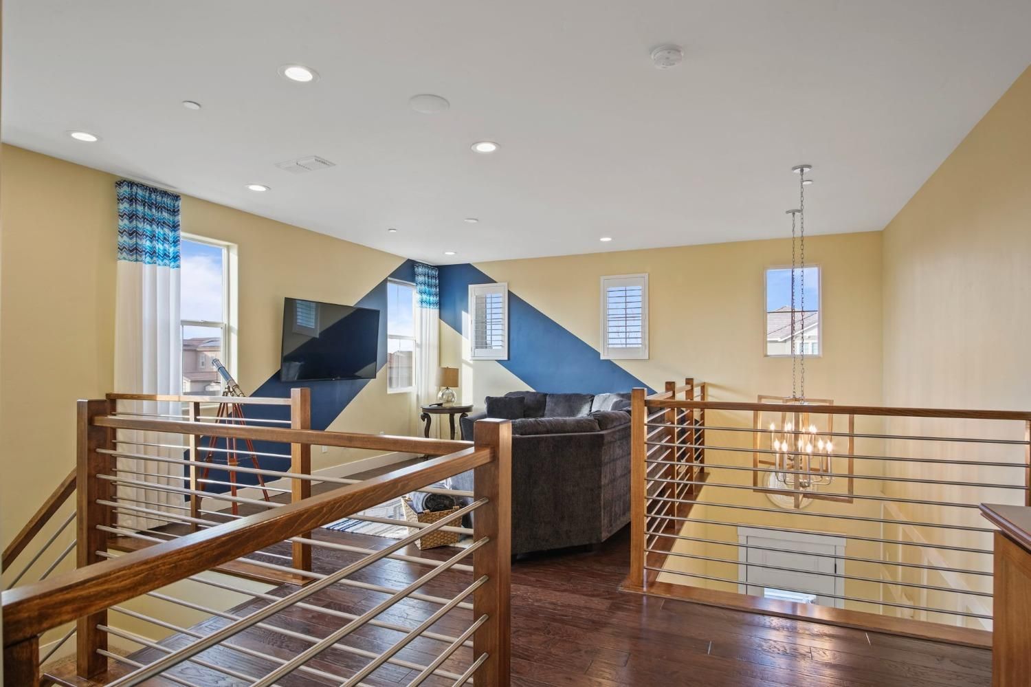 Open-concept loft with wooden railings, dark floors, and blue and yellow walls. A sofa and TV are visible.