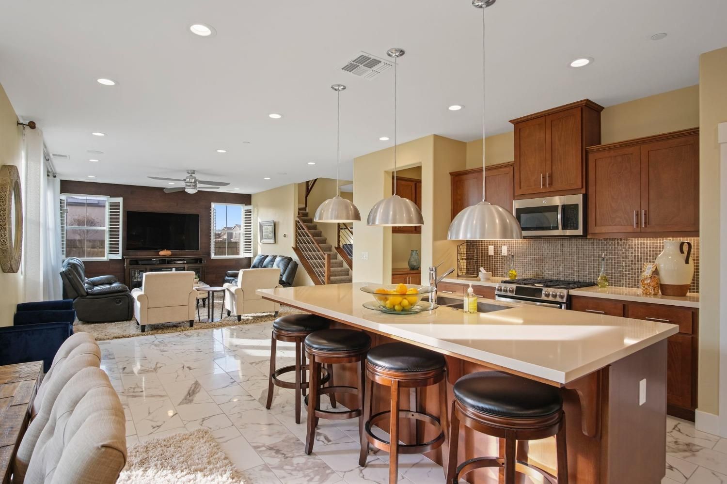 Open-concept kitchen with island and bar stools, leading into a living area with a dark TV and brown cabinets.