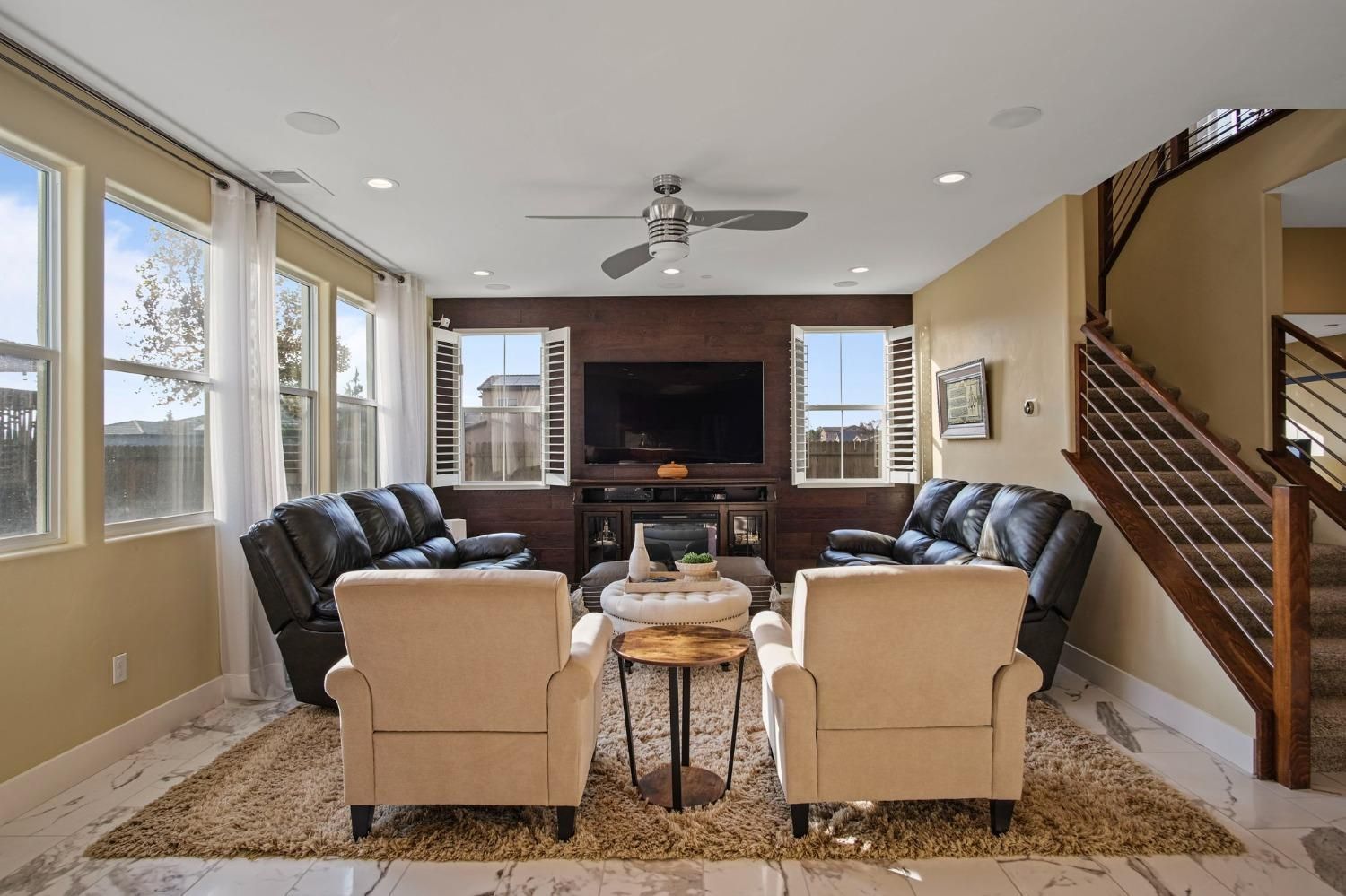 Living room with black sofas, cream chairs, TV, and stairs.