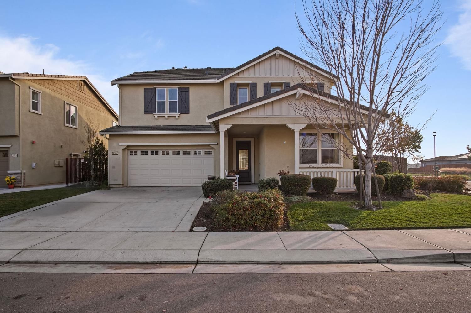 Two-story beige house with a garage and a small front porch, on a street with a blue sky.