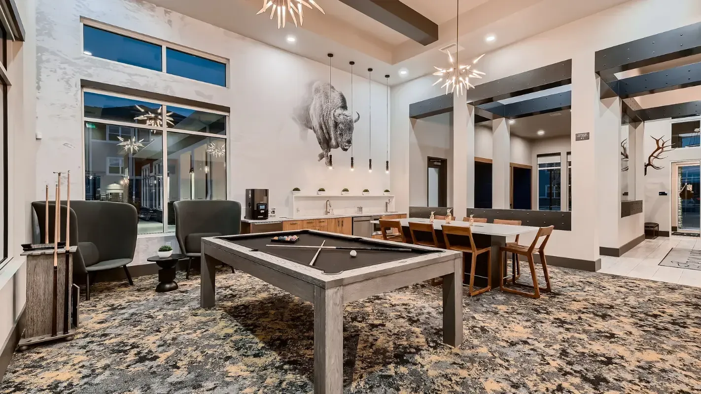 Interior view of a modern community lounge with a pool table, seating, and a kitchenette.