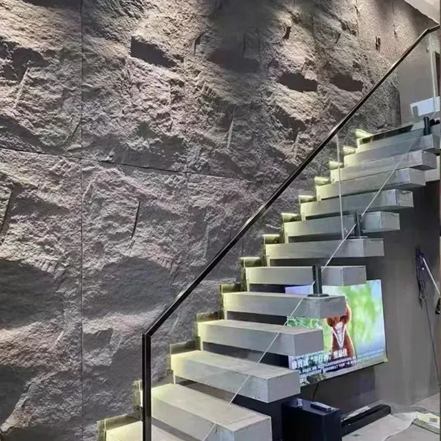 Una escalera con barandilla de cristal delante de un muro de piedra.
