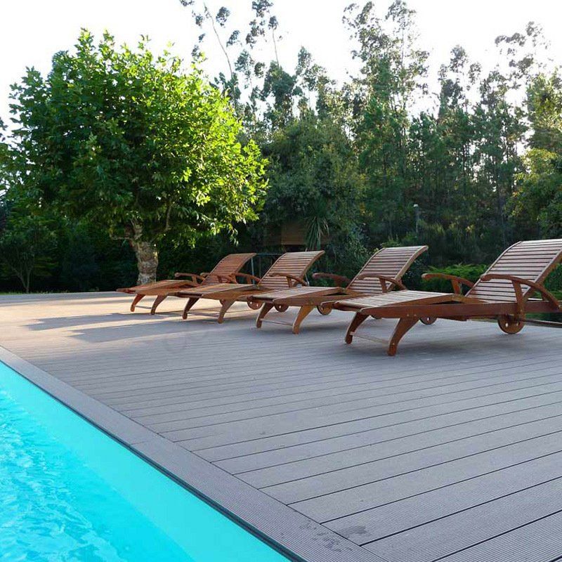 Una fila de sillas de madera en una terraza junto a una piscina.