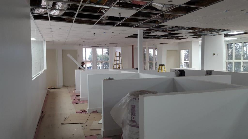 Office space under renovation with cubicles, exposed ceiling, and a worker.