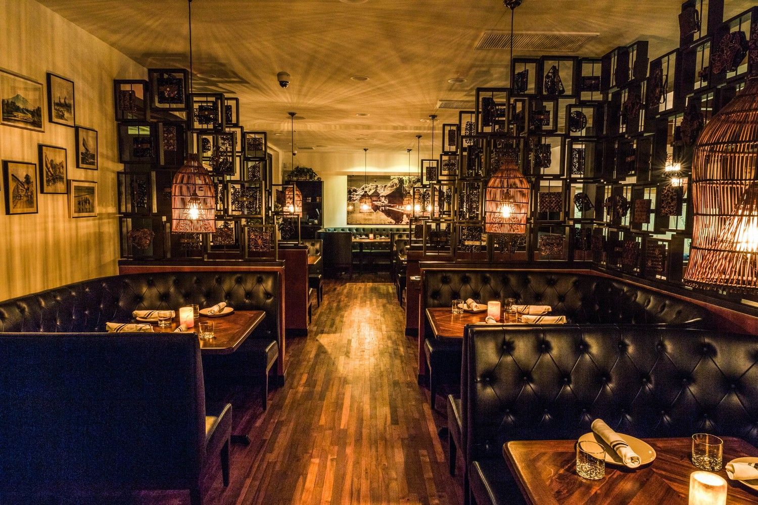 Dark restaurant interior with leather booths, wood tables, framed pictures on walls, and decorative hanging lights.