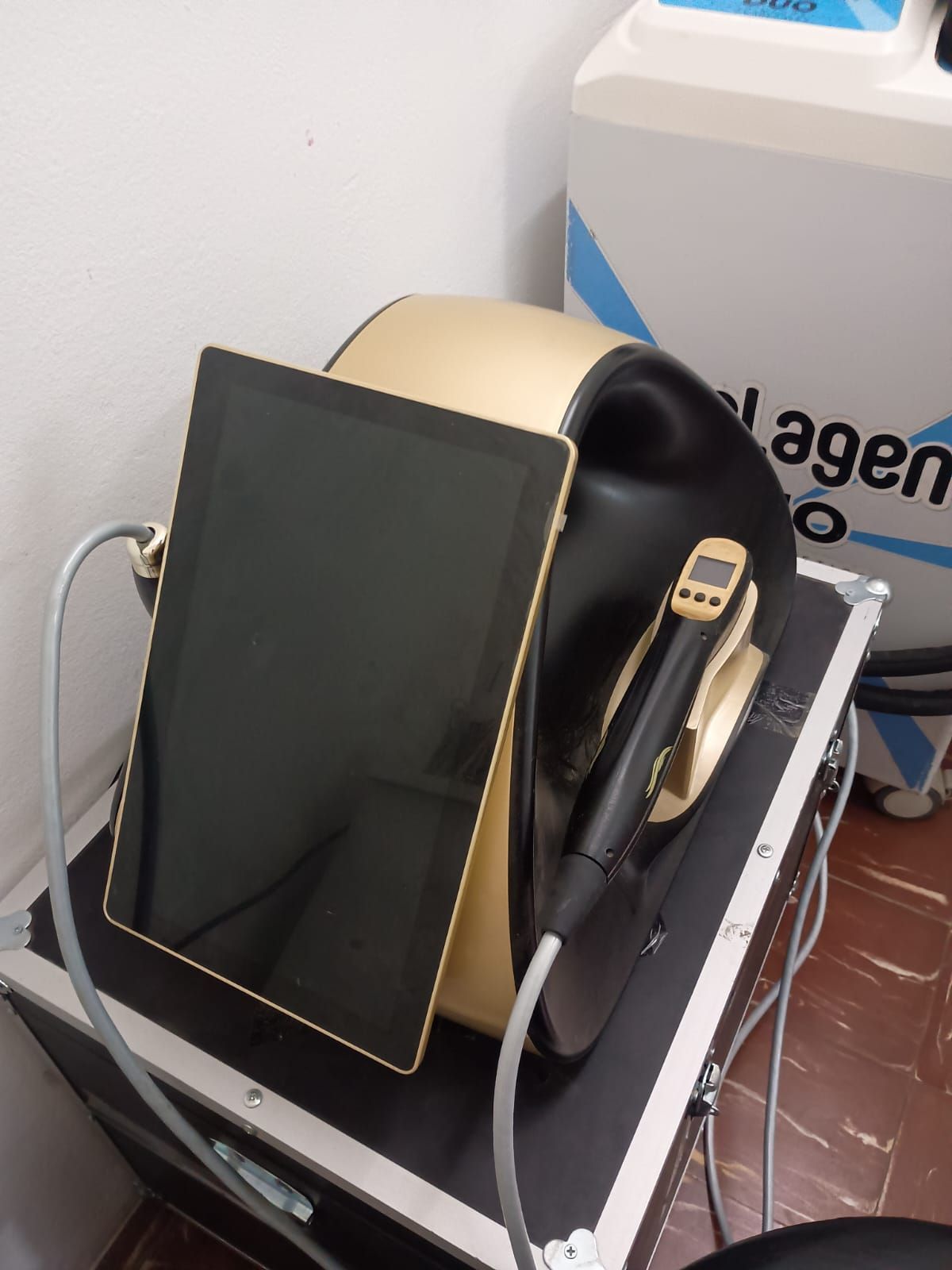 Pequeño aparato para tratamientos médicos/estéticos con cubierta negra y varita incorporada, sobre un carrito blanco