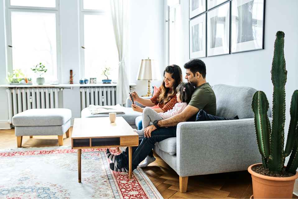 A family is sitting on a couch in a living room looking at a tablet.