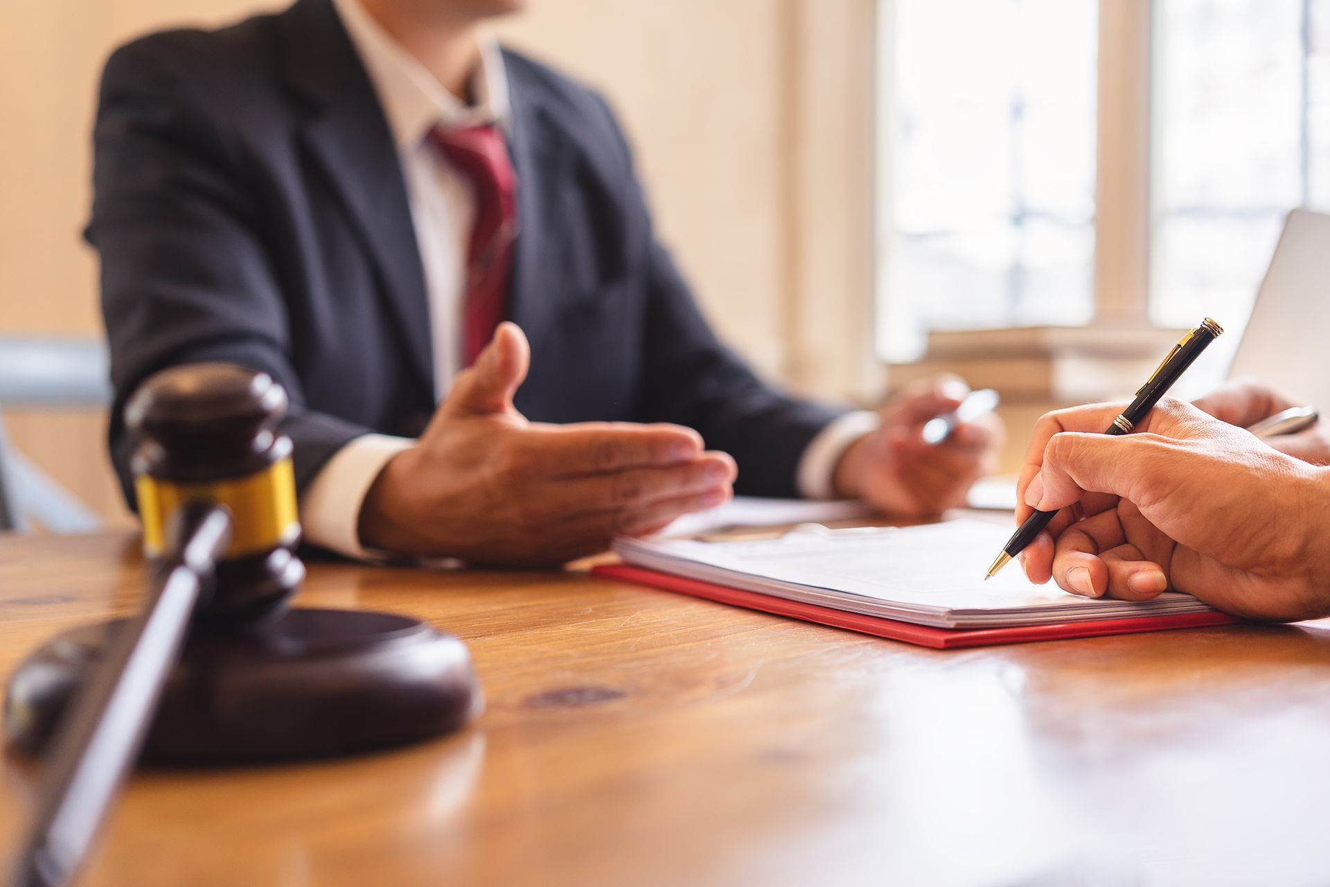 A lawyer and client engaged in a discussion, with documents and a laptop on the table between them.