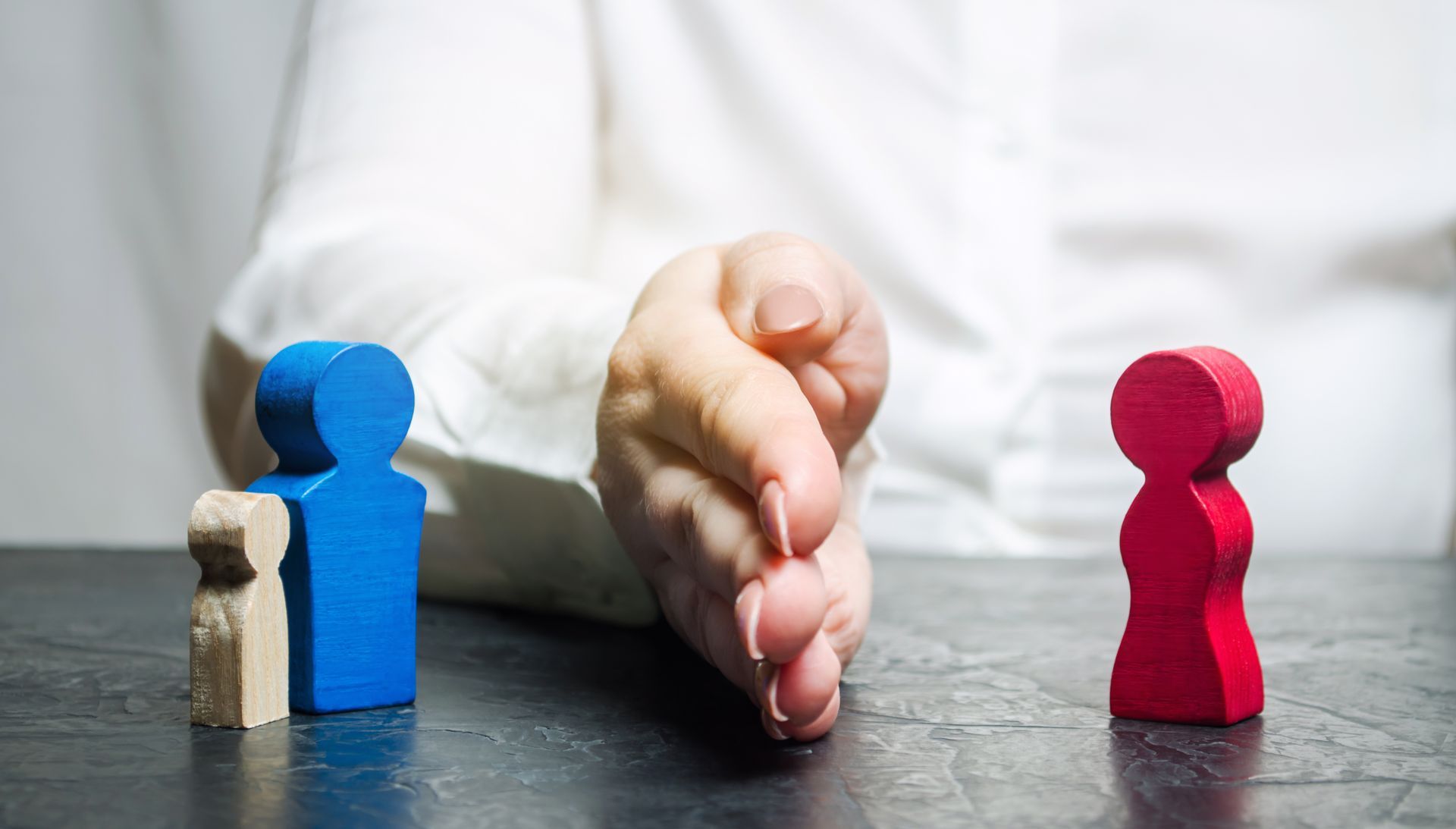A hand separates wooden figurines of a father with a child from the mother. A hand separates wooden figurines of a father with a child from the mother.