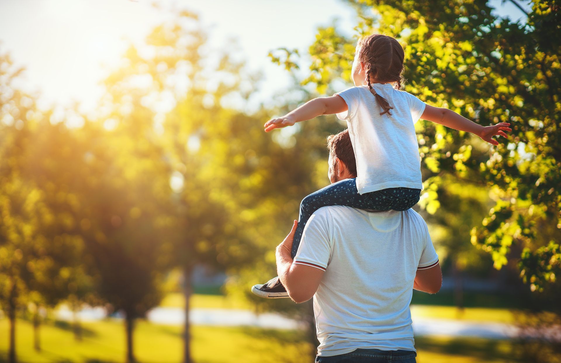 Father carrying daughter on his shoulders in a sunny park, representing fathers rights and parental bond Father carrying daughter on his shoulders in a sunny park, representing fathers rights and parental bond