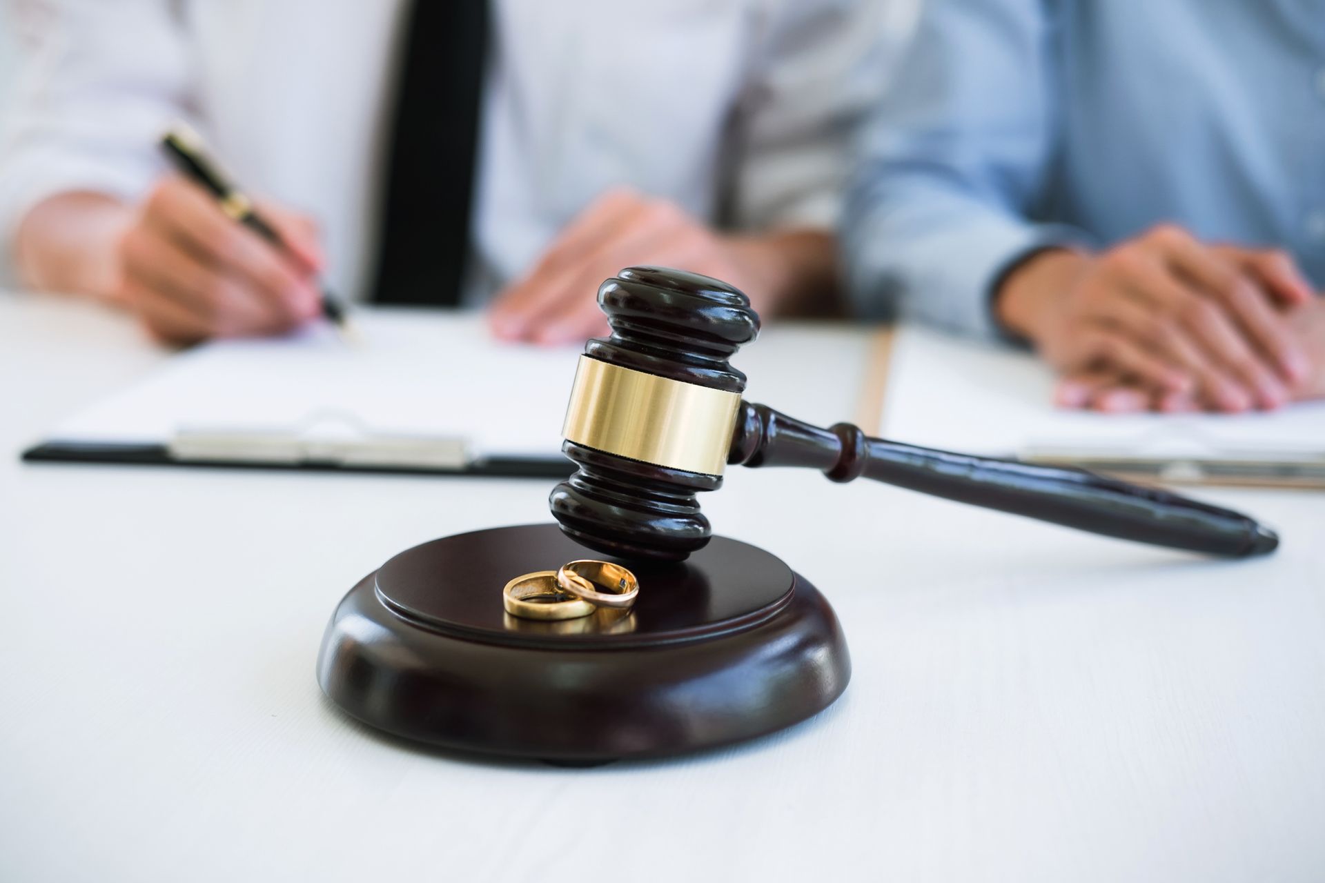 Wedding rings on a gavel with a man signing a paper, representing divorce lawyer services.