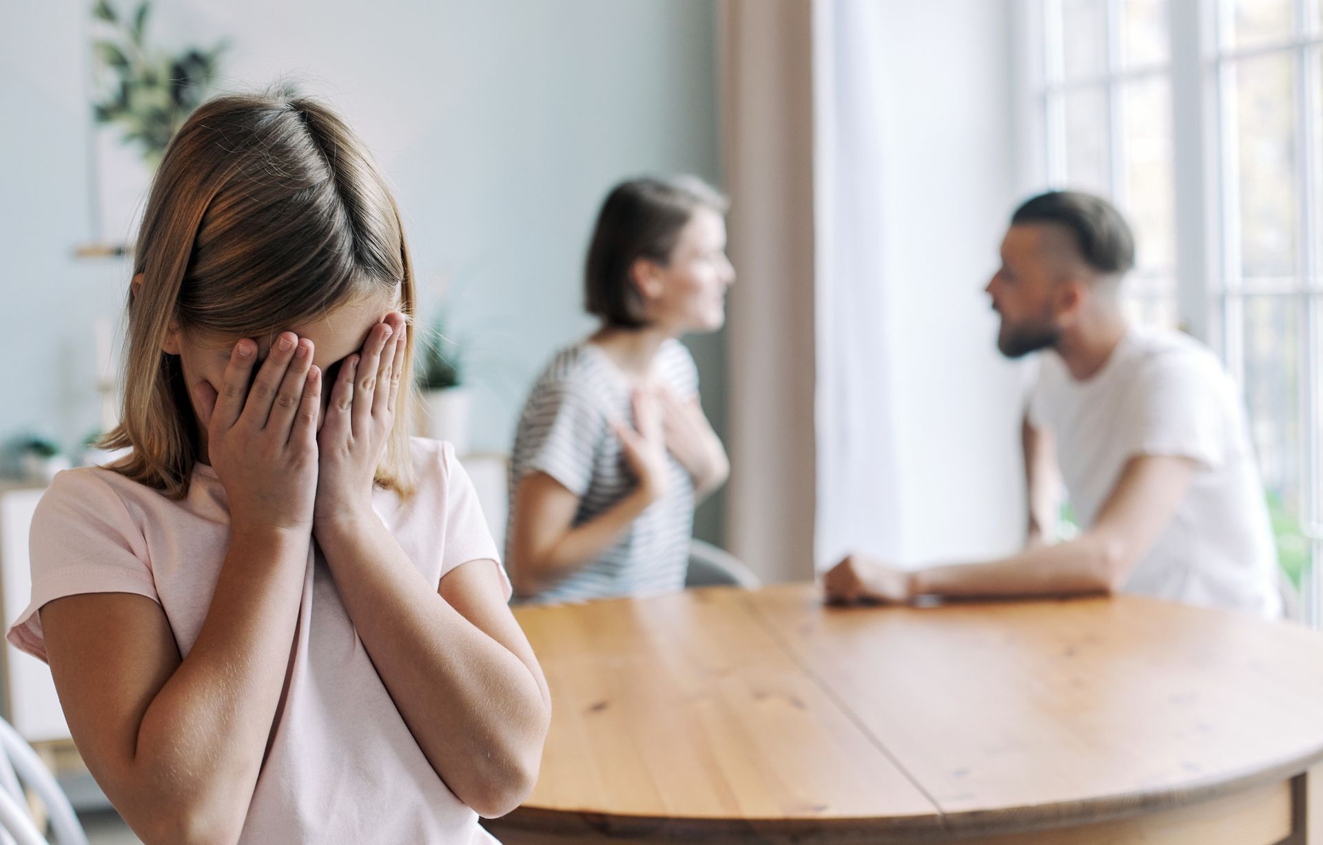 A couple arguing while their child covers her face.