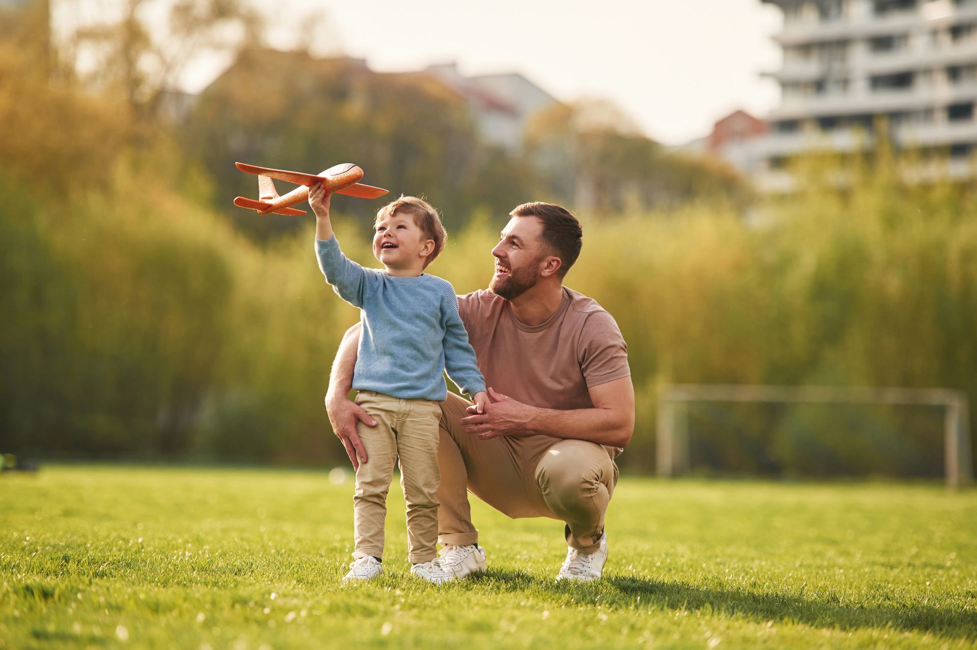 A father and son are playing with a toy airplane in a park.