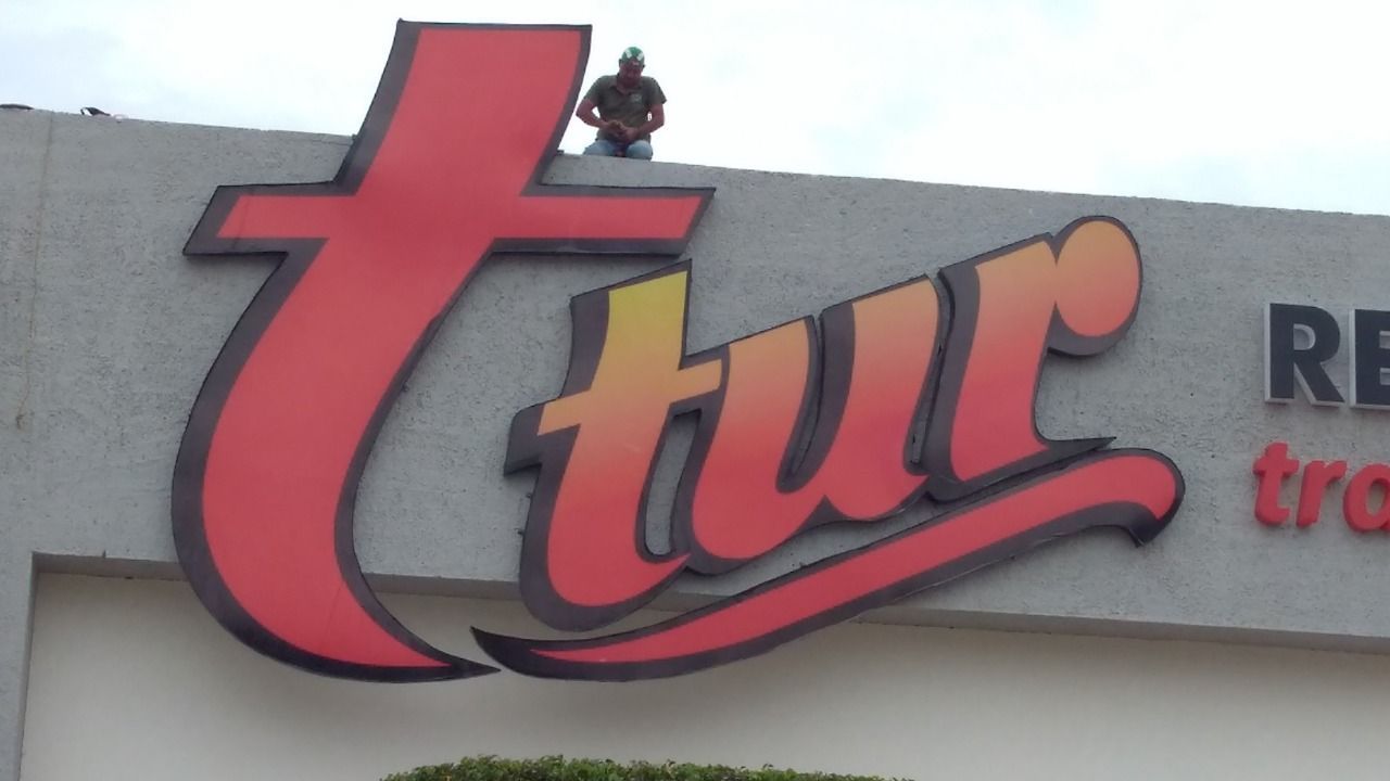 Un hombre se encuentra encima del cartel de un restaurante Tur.