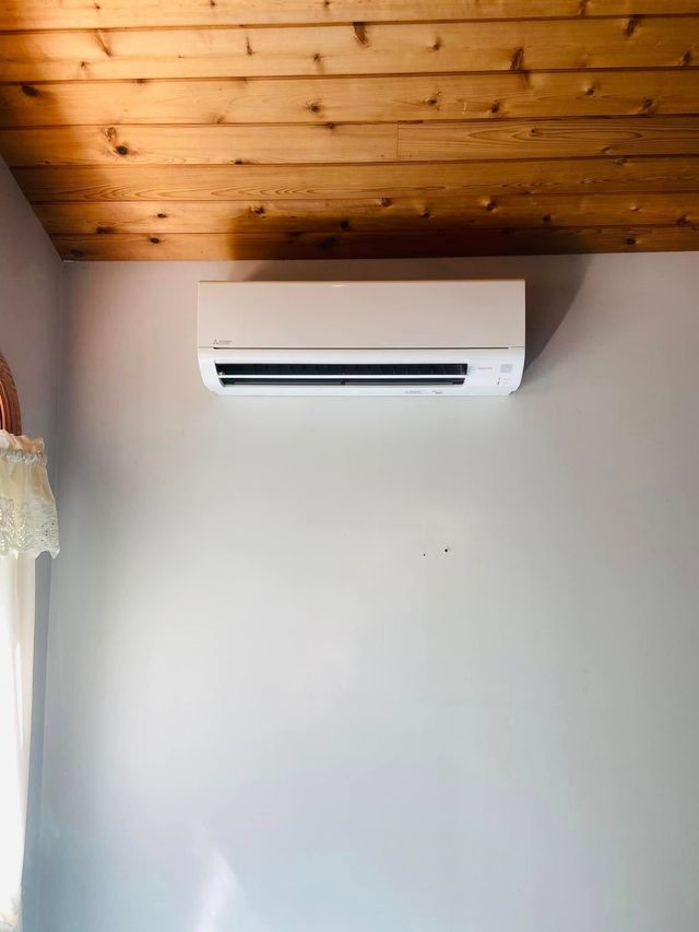 White wall with a wall-mounted air conditioner beneath a wooden plank ceiling.