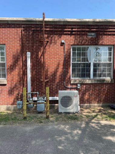 Red brick house exterior with utility pipes, an air conditioner unit, and a window with blinds.