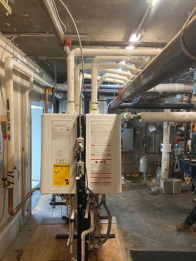 Industrial basement with exposed pipes and two wall-mounted control boxes in a mechanical room
