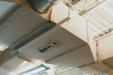 Ceiling air ducts and beams in a bright industrial interior, with a vent labeled “SUPPLY”