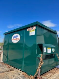 A green dumpster with a black tarp on top is parked on the side of the road.