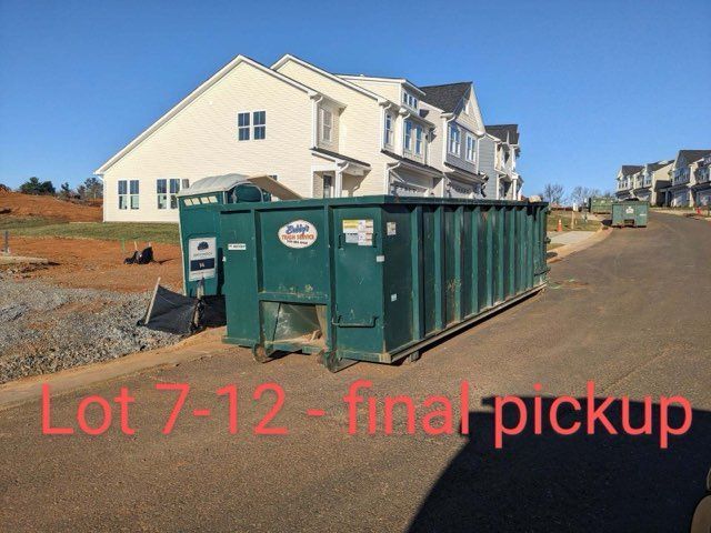 A green dumpster sits in front of a white house with the words lot 7-12 final pickup