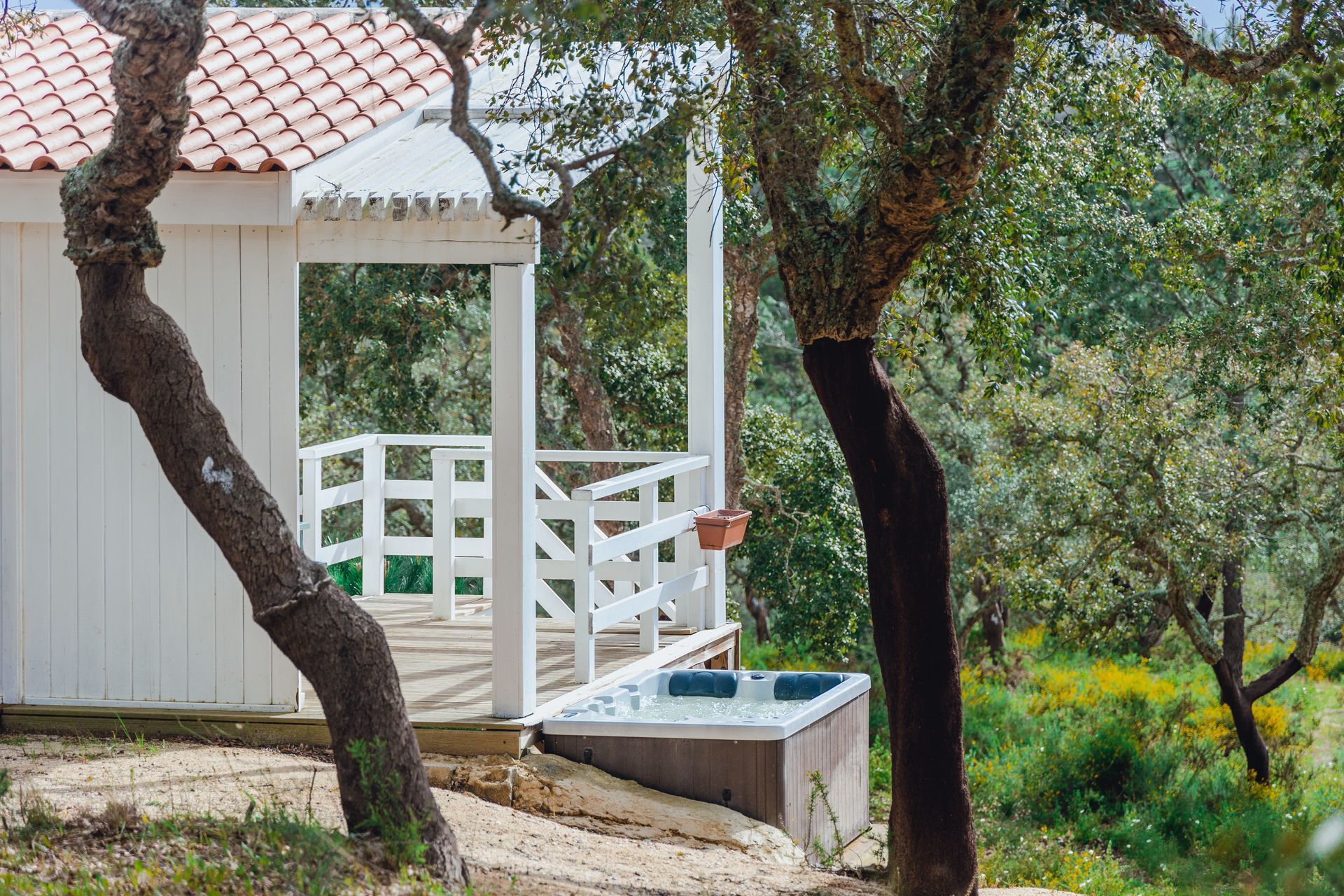 A small white house with a hot tub in front of it surrounded by trees.