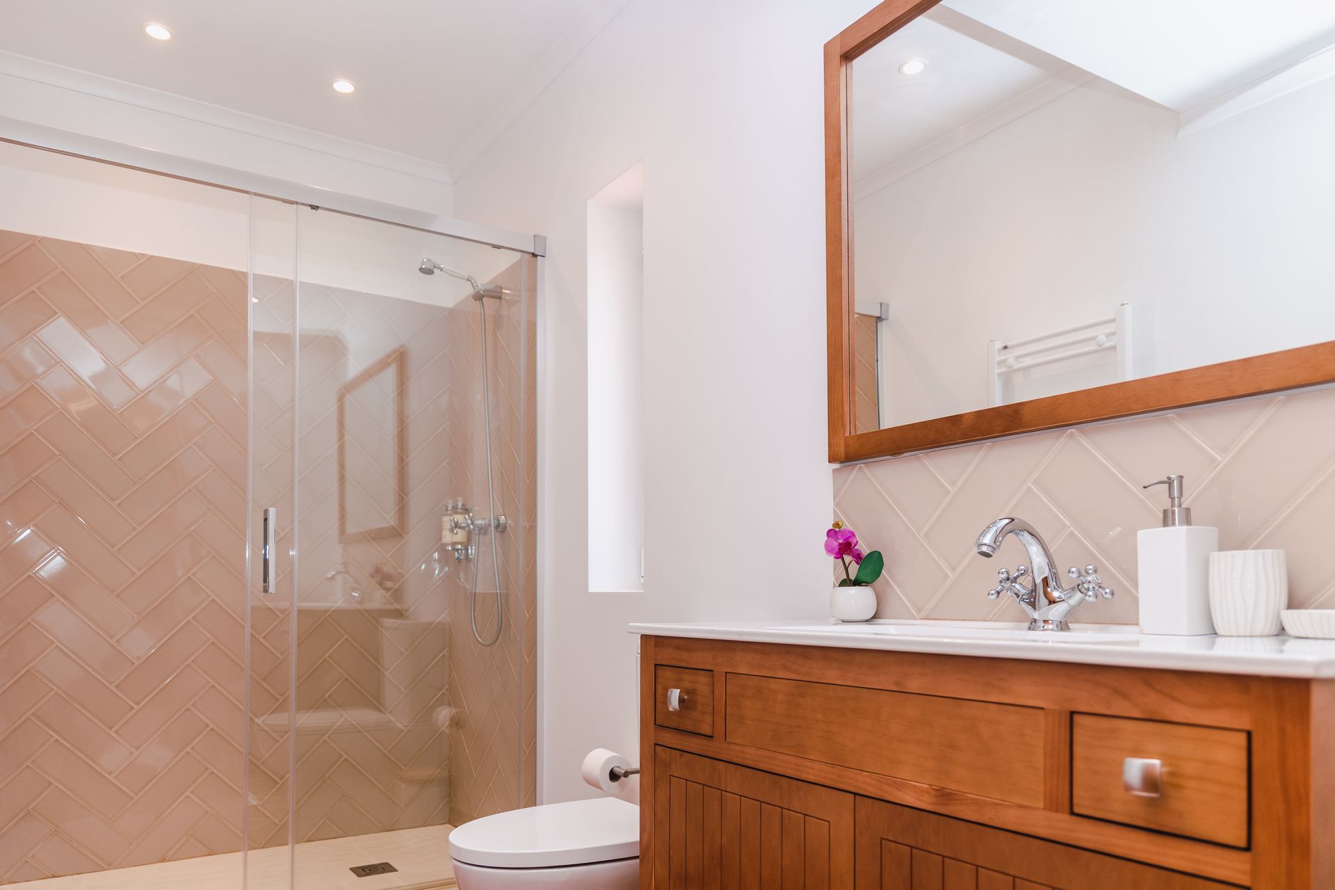 A bathroom with a toilet , sink , mirror and walk in shower.