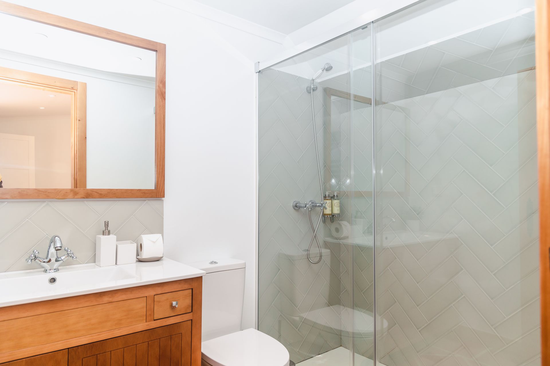 A bathroom with a toilet , sink , mirror and walk in shower.