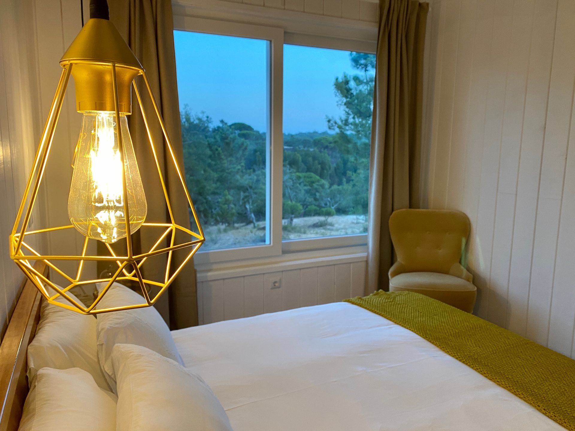A bedroom with a bed , chair , lamp and window.