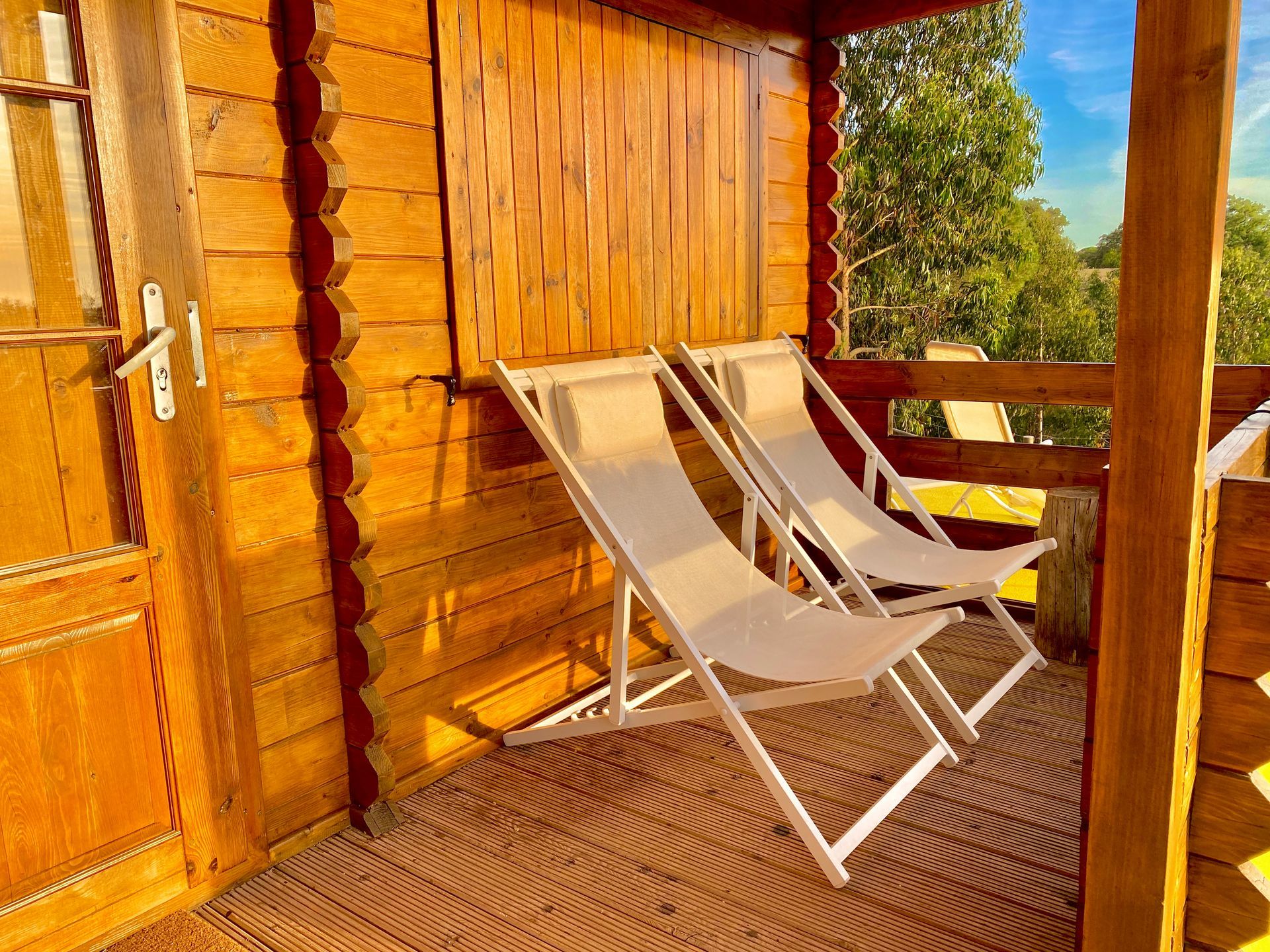 Two white folding chairs are sitting on a wooden porch.
