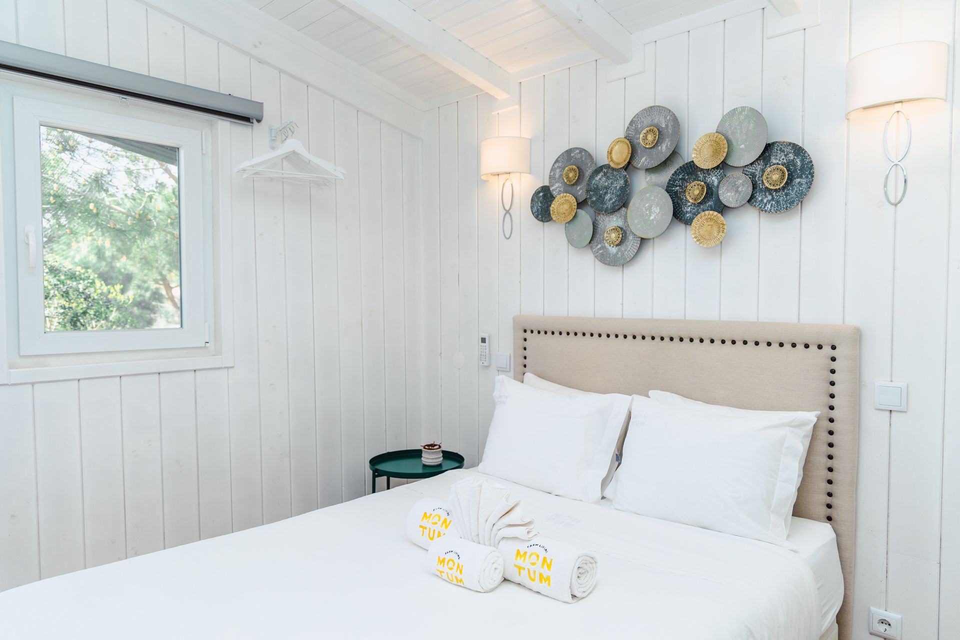 A bedroom with a bed and a window with a painting on the wall above the bed.