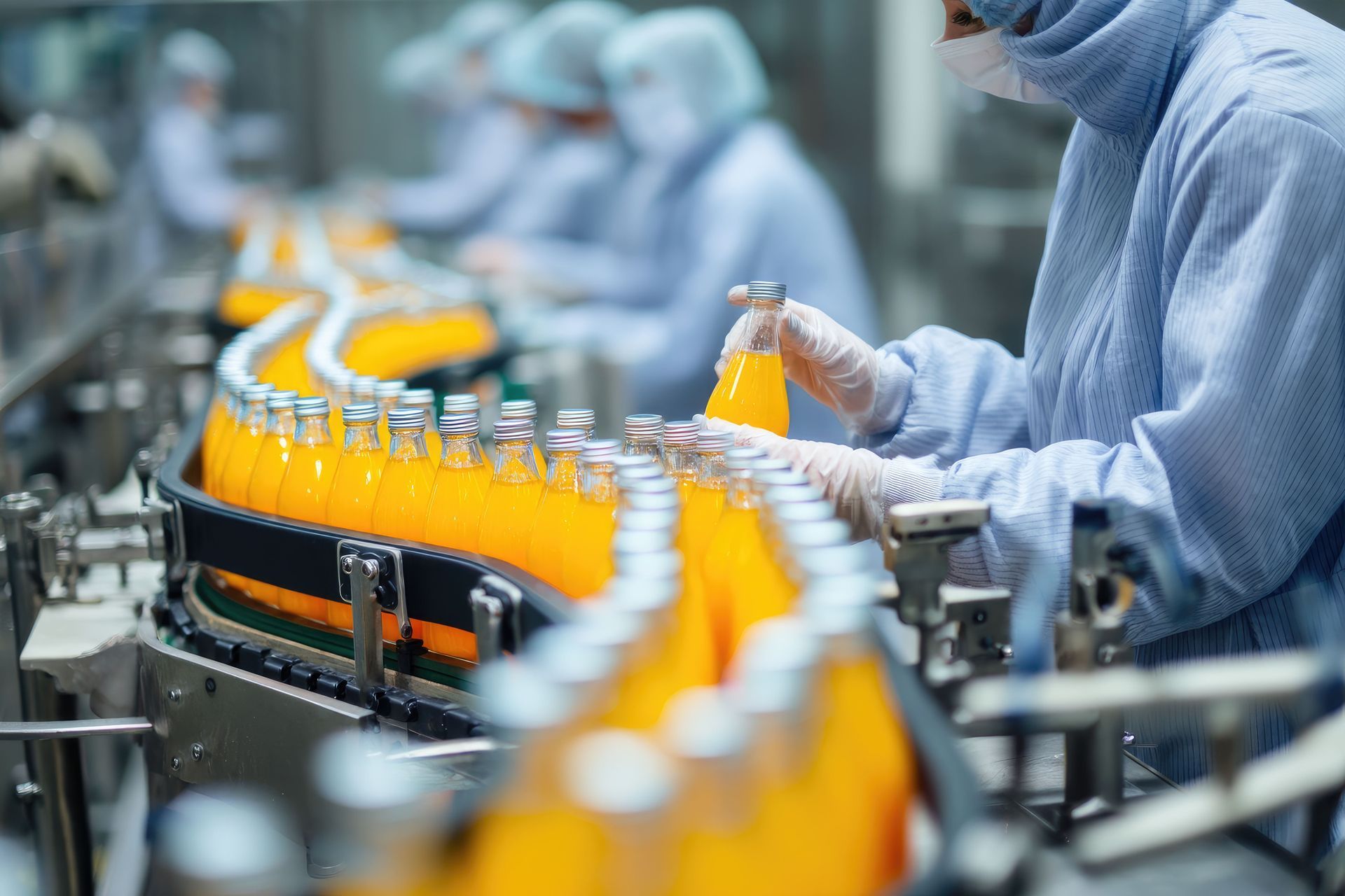 Bottles of orange juice on a conveyor belt, being handled by workers in protective suits.