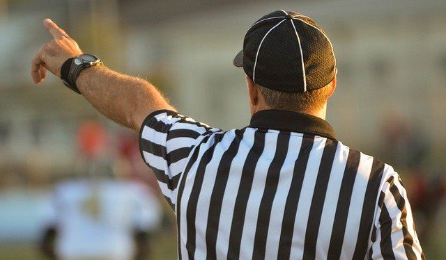 A referee wearing a black and white striped shirt is pointing at a player.