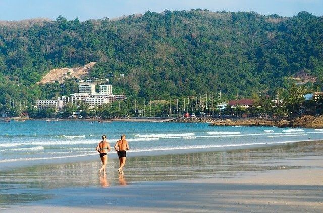 Two people are running on a beach with mountains in the background.